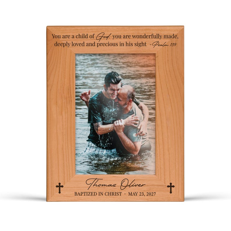 K&ouml;nnte beinhalten: Ein Holzfotorahmen mit einem Bild von zwei M&auml;nnern im Wasser, die sich umarmen. Der Rahmen hat Text oben und unten, darunter "You are a child of God" und "Thomas Oliver, Baptized in Christ, May 23, 2027". Kreuze sind auf dem Rahmen.