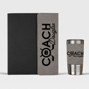 May include: A gray and black leatherette journal with the text "COACH Douglas" on the front cover. Next to the journal is a stainless steel travel mug with the same text on the side.