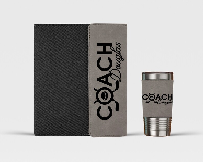 May include: A gray and black leatherette journal with the text "COACH Douglas" on the front cover. Next to the journal is a stainless steel travel mug with the same text on the side.