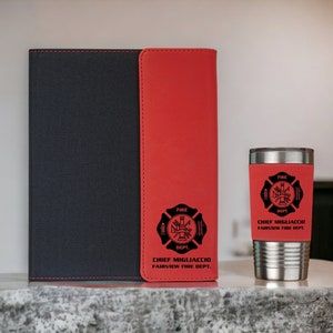 Pu&ograve; includere: Un taccuino nero con una striscia verticale rossa e un bicchiere in acciaio inossidabile abbinato. Entrambi gli articoli presentano un emblema nero dei vigili del fuoco con il testo "FIRE DEPT." e "CHIEF MIGLIACCIO FAIRVIEW FIRE DEPT." in nero.