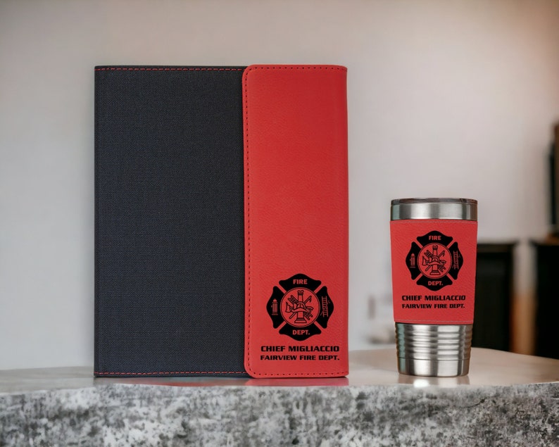 Pu&ograve; includere: Un taccuino nero con una striscia verticale rossa e un bicchiere in acciaio inossidabile abbinato. Entrambi gli articoli presentano un emblema nero dei vigili del fuoco con il testo "FIRE DEPT." e "CHIEF MIGLIACCIO FAIRVIEW FIRE DEPT." in nero.