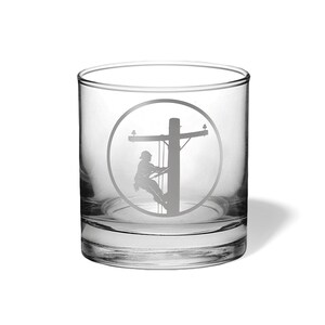 May include: A clear glass tumbler featuring an etched design of a utility worker climbing a wooden utility pole. The design is enclosed within a circular border, showcasing the silhouette of the worker and the pole structure in a frosted finish.