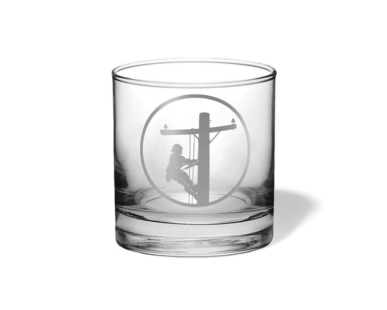 May include: A clear glass tumbler featuring an etched design of a utility worker climbing a wooden utility pole. The design is enclosed within a circular border, showcasing the silhouette of the worker and the pole structure in a frosted finish.