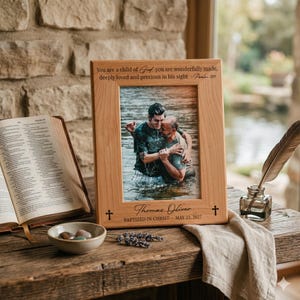 K&ouml;nnte beinhalten: Ein Bilderrahmen aus hellem Holz mit der Gravur 'You are a child of God you are wonderfully made, deeply loved and precious in his sight - Psalm 139' oben und 'Thomas Oliver BAPTIZED IN CHRIST MAY 23, 2027' am unteren Rand des Rahmens.