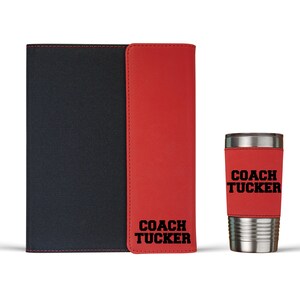 May include: A red and black leatherette journal with the text "COACH TUCKER" on the front cover. A red and silver tumbler with the same text is also included.