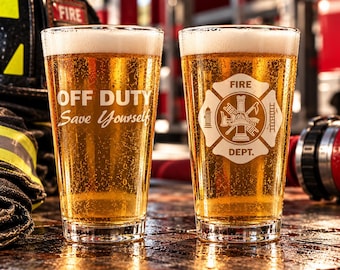 May include: Two clear glass pint glasses filled with golden beer. The left glass features the white text OFF DUTY Save Yourself. The right glass displays a white fire department emblem with a central helmet, ladder, and hydrant icon.