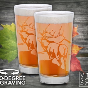 Puede incluir: Dos jarras de cerveza de vidrio transparente con un dise&ntilde;o esmerilado de un alce con cuernos. Las jarras est&aacute;n llenas de una cerveza de color &aacute;mbar claro. El texto "360-DEGREE ENGRAVING" est&aacute; en la parte inferior de la imagen. El texto "VITAL SIGNS NORTHWEST" est&aacute; en la parte inferior derecha de la imagen.