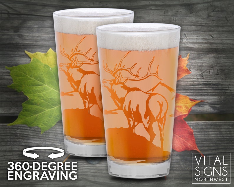 Puede incluir: Dos jarras de cerveza de vidrio transparente con un dise&ntilde;o esmerilado de un alce con cuernos. Las jarras est&aacute;n llenas de una cerveza de color &aacute;mbar claro. El texto "360-DEGREE ENGRAVING" est&aacute; en la parte inferior de la imagen. El texto "VITAL SIGNS NORTHWEST" est&aacute; en la parte inferior derecha de la imagen.