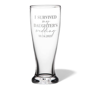 May include: A clear glass beer pilsner featuring the etched text I SURVIVED my DAUGHTER'S wedding 10.14.2023. The glass has a tapered cylindrical shape with a thick, weighted base and a smooth, transparent finish throughout the entire vessel.