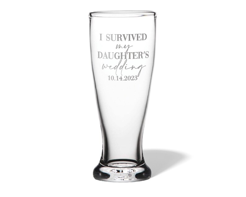 May include: A clear glass beer pilsner featuring the etched text I SURVIVED my DAUGHTER'S wedding 10.14.2023. The glass has a tapered cylindrical shape with a thick, weighted base and a smooth, transparent finish throughout the entire vessel.