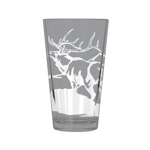 Puede incluir: Un vaso de vidrio transparente con un tinte gris presenta un dise&ntilde;o grabado en blanco de un alce de pie en un paisaje de monta&ntilde;a.