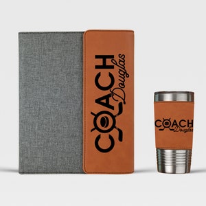 May include: A brown leatherette folder with a gray fabric cover and the text "COACH Douglas" in black. Next to it is a brown leatherette insulated tumbler with the same text.
