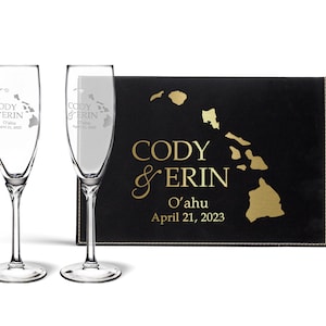 May include: Two champagne flutes with a gold outline of the Hawaiian islands and the text "Cody & Erin O'ahu April 21, 2023" etched into the glass. The flutes are in a black box with a gold outline of the Hawaiian islands and the text "Cody & Erin O'ahu April 21, 2023".