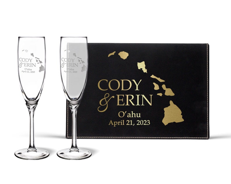 May include: Two champagne flutes with a gold outline of the Hawaiian islands and the text "Cody & Erin O'ahu April 21, 2023" etched into the glass. The flutes are in a black box with a gold outline of the Hawaiian islands and the text "Cody & Erin O'ahu April 21, 2023".