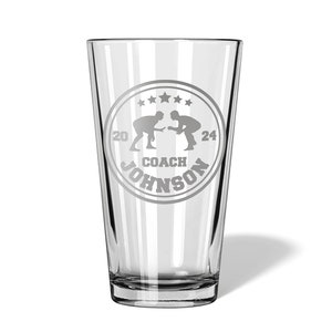 May include: A clear glass pint glass with a white etched design of two wrestlers in a circle with the text "COACH JOHNSON" and stars around the circle.