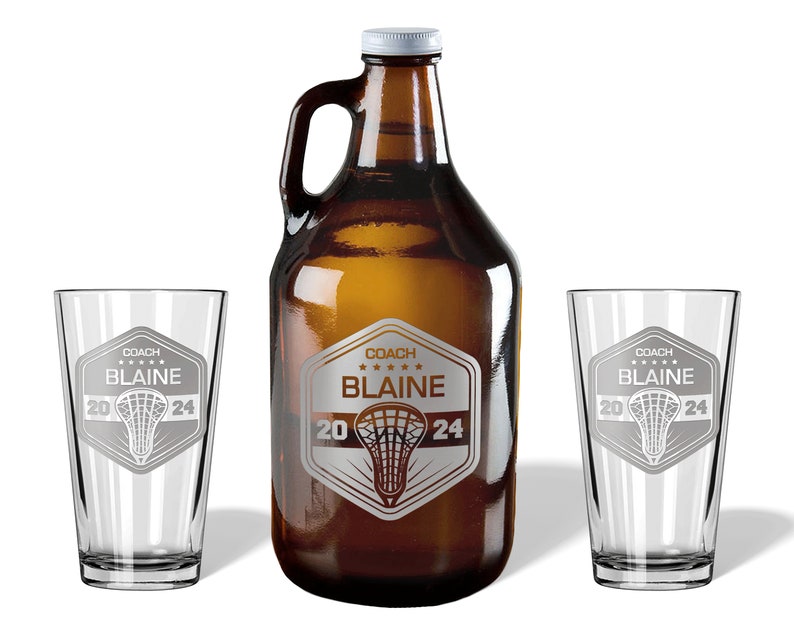May include: A brown glass growler and two clear pint glasses. Each glass and the growler feature a silver emblem with the text "COACH BLAINE 2024" and a lacrosse stick design. The growler has a white cap.