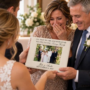 May include: A rectangular off-white picture frame with stitched edges, featuring the text "ALL THAT WE ARE AND HOPE TO BE WE OWE TO OUR Loving Family" at the top and "Jake & Amber SEPTEMBER 14, 2027" at the bottom, holding a wedding photo.