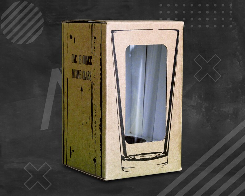 May include: A tall, clear mixing glass is visible through a rectangular window in a cardboard box. The box is printed with the text "ONE 16 OUNCE MIXING GLASS". The box has a rustic, distressed appearance.