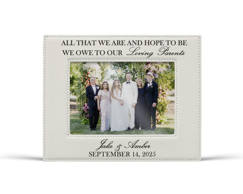 May include: A rectangular off-white leatherette picture frame featuring stitched borders. The top text reads ALL THAT WE ARE AND HOPE TO BE WE OWE TO OUR Loving Parents. The bottom text reads Jake & Amber SEPTEMBER 14, 2025.