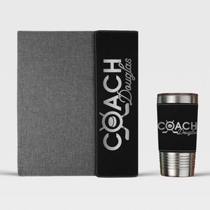 May include: A black and gray notebook with a black and silver "COACH Douglas" logo on the cover. Next to the notebook is a silver tumbler with a black and silver "COACH Douglas" logo on the sleeve.