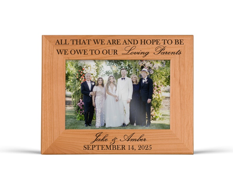 May include: A light brown wooden picture frame featuring the engraved text ALL THAT WE ARE AND HOPE TO BE WE OWE TO OUR Loving Parents at the top and Jake & Amber SEPTEMBER 14, 2025 at the bottom, holding a wedding photograph.