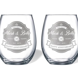 May include: Two clear glass wine glasses with a silver design that says "Finest Quality Mark & Betty Aged 50 Years Est 1972 Happy Anniversary".