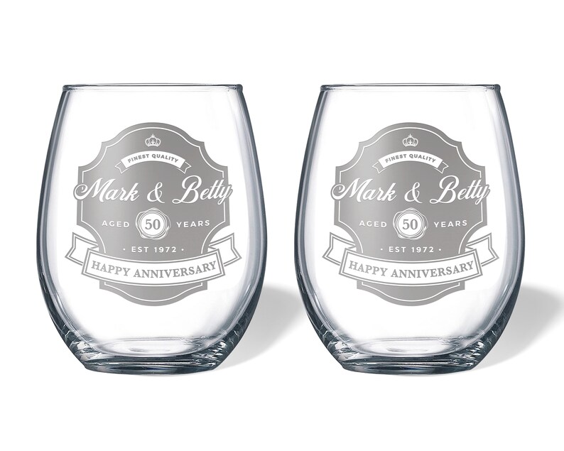 May include: Two clear glass wine glasses with a silver design that says "Finest Quality Mark & Betty Aged 50 Years Est 1972 Happy Anniversary".