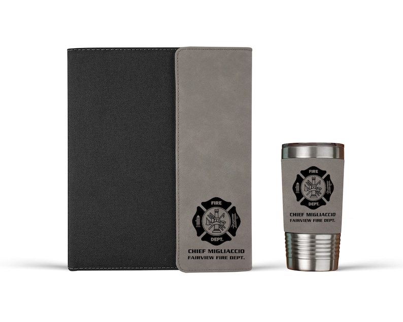 Pu&ograve; includere: Un taccuino nero con un pannello verticale grigio e un bicchiere in acciaio inossidabile grigio abbinato. Entrambi gli articoli presentano un emblema nero dei vigili del fuoco con il testo "CHIEF MIGLIACCIO FAIRVIEW FIRE DEPT." sulle superfici grigie.