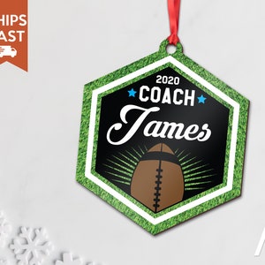 May include: A green and black hexagonal Christmas ornament with a white border. The ornament features a football, the text "2020 COACH James" and two blue stars.