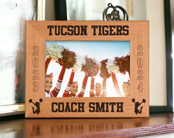 May include: A wooden photo frame with the text "TUCSON TIGERS" and "COACH SMITH" engraved on it. The frame holds a photo of cheerleaders with red and white pom-poms. The years 2023 and 2024 are also engraved on the frame.