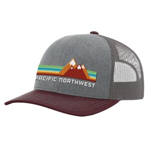 May include: A gray and burgundy trucker hat with a mesh back. The front of the hat features a graphic of mountains with a sunset and the text "PACIFIC NORTHWEST".