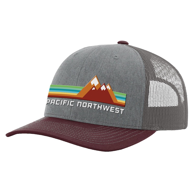 May include: A gray and burgundy trucker hat with a mesh back. The front of the hat features a graphic of mountains with a sunset and the text "PACIFIC NORTHWEST".