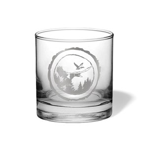 May include: A clear glass tumbler with a design of a duck flying over a forest scene etched into the side. The design is in a circle with a wood grain texture.