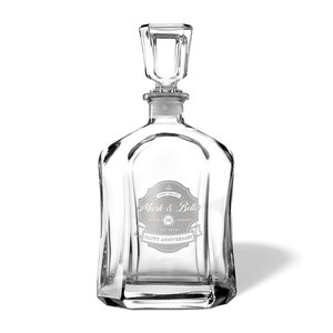 May include: A clear glass decanter with a stopper and a personalized label that reads "Mark & Bella, 50 Years, Est. 1973, Happy Anniversary".