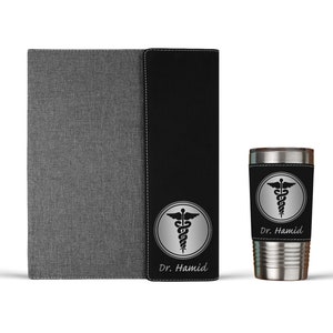 K&ouml;nnte beinhalten: Ein personalisiertes Notizbuch in Schwarz und Grau und ein Edelstahlbecher mit einem schwarzen und silbernen medizinischen Symbol und dem Namen "Dr. Hamid" auf beiden Artikeln.