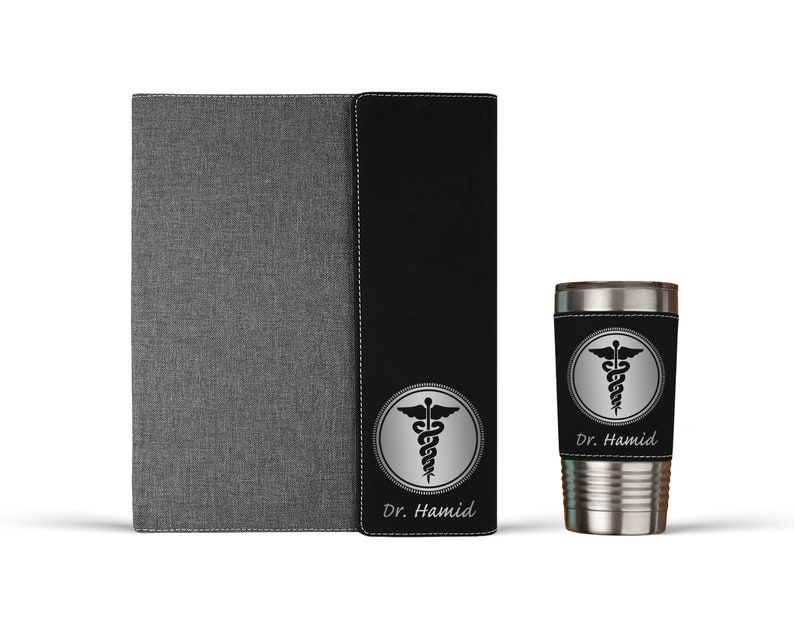 K&ouml;nnte beinhalten: Ein personalisiertes Notizbuch in Schwarz und Grau und ein Edelstahlbecher mit einem schwarzen und silbernen medizinischen Symbol und dem Namen "Dr. Hamid" auf beiden Artikeln.