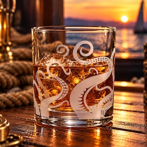 May include: A clear glass tumbler featuring an etched white design of octopus tentacles wrapping around the exterior. The glass is filled with an amber-colored liquid and several ice cubes, showcasing the detailed suction cup patterns.