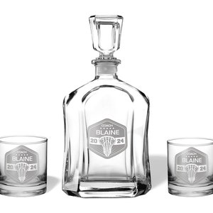 May include: A clear glass decanter set with two matching lowball glasses. The decanter has a square stopper. Each piece is etched with a lacrosse graphic and the text "COACH BLAINE 2024".