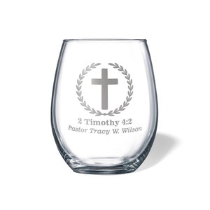 May include: A clear glass wine glass with a silver etched design of a cross inside a wreath. The text "2 Timothy 4:2 Pastor Tracy W. Wilson" is also etched on the glass.