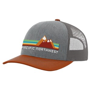 May include: A gray and orange trucker hat with a red mountain range graphic and the text "PACIFIC NORTHWEST" in white.