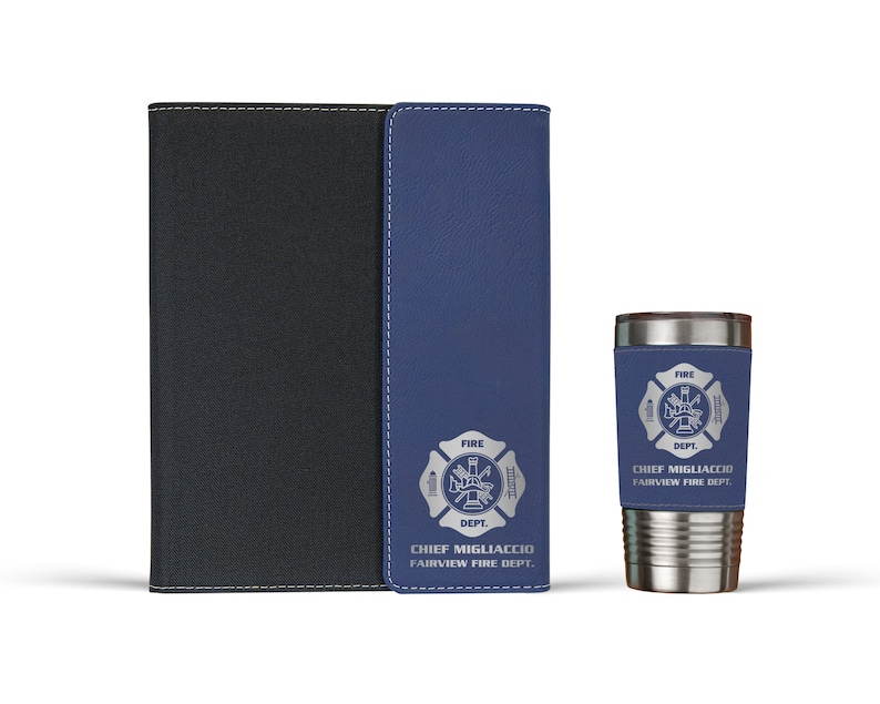 Pu&ograve; includere: Un taccuino nero e blu con cuciture bianche e un emblema argentato dei vigili del fuoco con il testo CHIEF MIGLIACCIO FAIRVIEW FIRE DEPT. Accanto c'&egrave; un bicchiere in acciaio inossidabile con una fascia blu abbinata e lo stesso emblema.