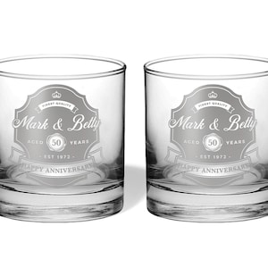 May include: Two clear glass tumblers with a silver etched design. The design features a banner with the text "Mark & Betty" and "Happy Anniversary". The banner also includes the text "Aged 50 Years" and "Est 1972".