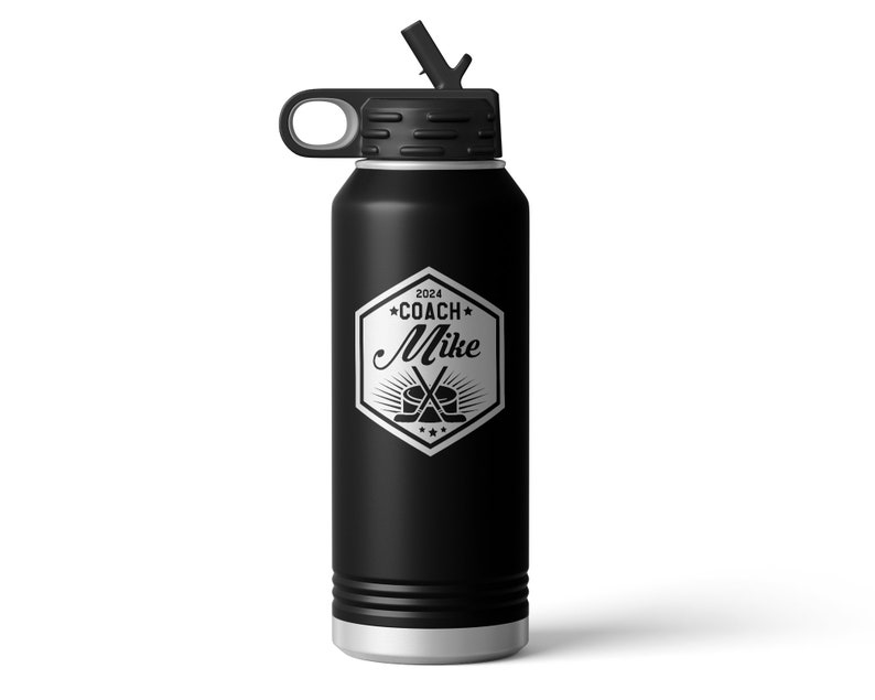 May include: A matte black insulated water bottle with a silver base and a black lid featuring a straw. The front displays a silver hexagonal emblem with the text 2024 COACH Mike, accompanied by a graphic of a hockey puck and two crossed sticks.