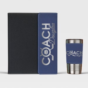 May include: A blue and black leatherette notebook with the text "COACH Douglas" in silver lettering. A silver stainless steel tumbler with a blue leatherette sleeve with the text "COACH Douglas" in silver lettering.