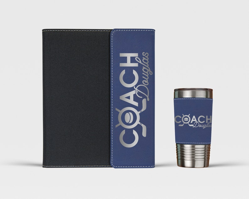 May include: A blue and black leatherette notebook with the text "COACH Douglas" in silver lettering. A silver stainless steel tumbler with a blue leatherette sleeve with the text "COACH Douglas" in silver lettering.
