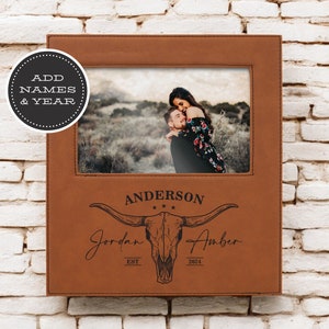 May include: A brown leather photo frame with a skull and crossbones design. The frame has a cutout for a photo and is engraved with the text "Anderson", "Jordan", "Amber", "Est", and "2024".