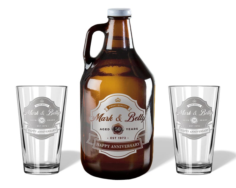 May include: A 64-ounce glass growler with a brown glass bottle and two matching pint glasses. The growler and glasses are engraved with the text "Mark & Betty Aged 50 Years Est 1972 Happy Anniversary".