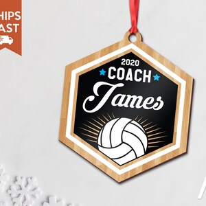 May include: A wooden hexagon-shaped ornament with a black background and a white volleyball. The ornament has the text "2020 COACH James" in white with blue stars.