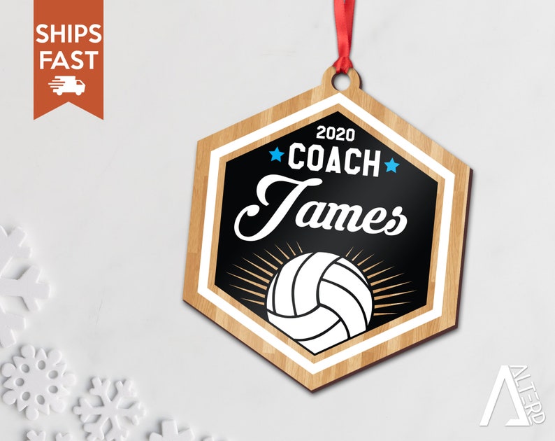 May include: A wooden hexagon-shaped ornament with a black background and a white volleyball. The ornament has the text "2020 COACH James" in white with blue stars.