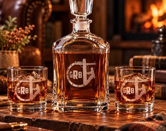 May include: A clear glass decanter with a matching stopper and two matching whiskey glasses, all filled with amber liquid. Each piece features an etched circular logo containing the letters GRB and a silhouette of a utility pole worker.